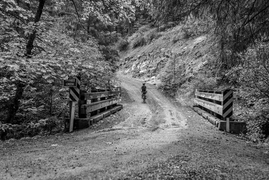 Gravel cyclist riding a dirt road through a wooded canyon, Hudson Valley style terrain